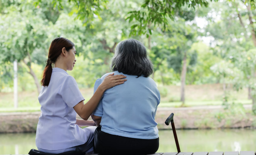 A compassionate nurse comforting an elderly woman sitting by a lake, representing Medicare hospice support in Colorado.